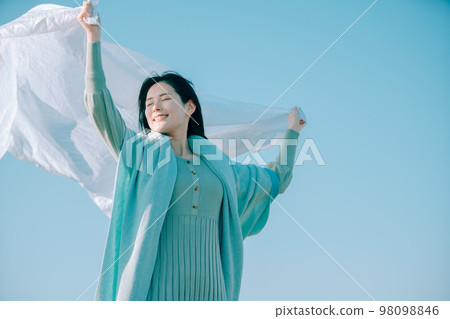 A woman in her twenties who is immersed in a sense of openness with the blue sky in the background A woman in her twenties who is immersed in a sense of openness with the blue sky in the background 98098846