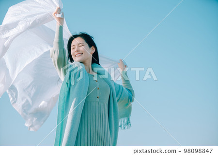 A woman in her twenties who is immersed in a sense of openness with the blue sky in the background A woman in her twenties who is immersed in a sense of openness with the blue sky in the background 98098847