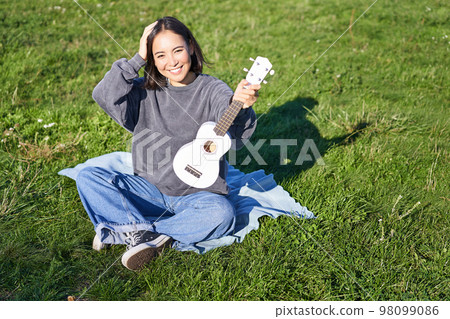 Excited asian girl sits in park with ukulele, plays instrument and feels happy upbeat, positive moments and people concept Excited asian girl sits in park with ukulele, plays instrument and feels happy upbeat, positive moments and people concept 98099086