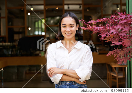 Young asian woman, cafe owner or manager, standing confident with arms crossed on hands, smiling and looking at camera Young asian woman, cafe owner or manager, standing confident with arms crossed on hands, smiling and looking at camera 98099115