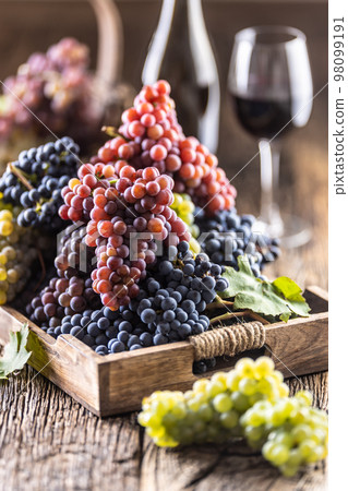 Juicy bunches of grapes in a wooden box, red wine in the background 98099191