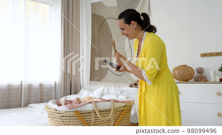Mother playing with baby by using rattle toy and taking photos of it on smartphone 98099496