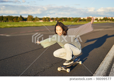Freedom and happiness. Happy asian girl riding her longboard on an empty sunny road, laughing and smiling, skateboarding Freedom and happiness. Happy asian girl riding her longboard on an empty sunny road, laughing and smiling, skateboarding 98099577