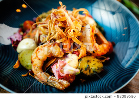 Warm salad with Argentinian king prawns. Almond potato, mini romaine lettuce, carrot, cherry tomato, pesto, black root chips, caramelized walnut, beet balsamic. Food served in modern restaurant 98099580