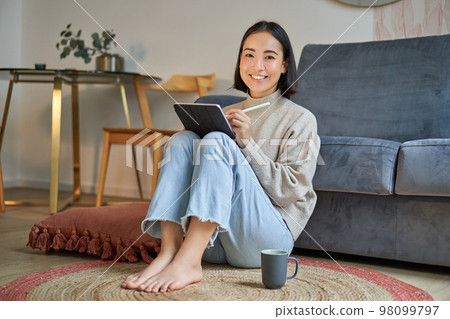 Portrait of creative young woman drawing on digital tablet with pen, drinking coffee, working from home, plan and design new project Portrait of creative young woman drawing on digital tablet with pen, drinking coffee, working from home, plan and design new project 98099797