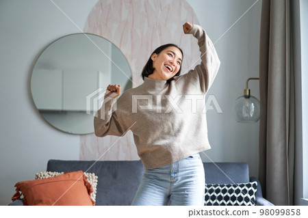 Portrait of happy asian woman dancing, rejoicing and triumphing, feeling upbeat at home Portrait of happy asian woman dancing, rejoicing and triumphing, feeling upbeat at home 98099858