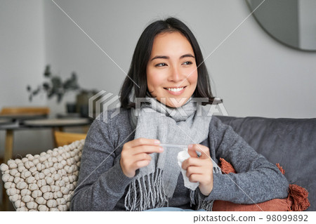 Smiling asian woman holding thermometer and looking pleased, feeling better after cold, got rid of fever, has normal temperature 98099892