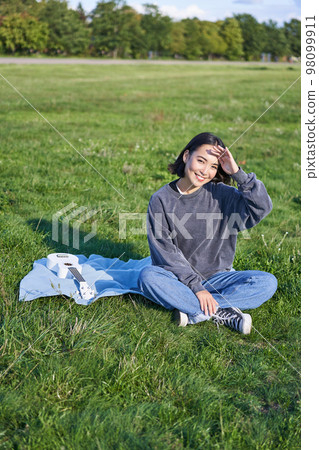Beautiful asian girl, musician sitting in park and playing ukulele, smiling happy at camera. Lifestyle and young people concept 98099911