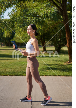 Active asian girl, in fitness clothing, workout in park, walking in sportswear with smartphone and water bottle Active asian girl, in fitness clothing, workout in park, walking in sportswear with smartphone and water bottle 98099973