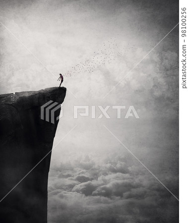 Freedom and liberty conceptual scene. Man on the edge of a cliff self liberating from fears and doubts as a flock of birds escape his body and fly free in the air. Surreal and inspirational art 98100256