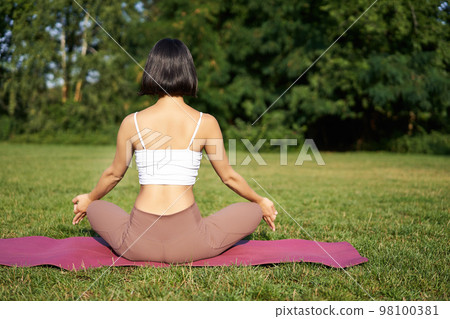 Rear view of woman silhouette doing yoga, sitting on fitness mat and meditating on green lawn Rear view of woman silhouette doing yoga, sitting on fitness mat and meditating on green lawn 98100381