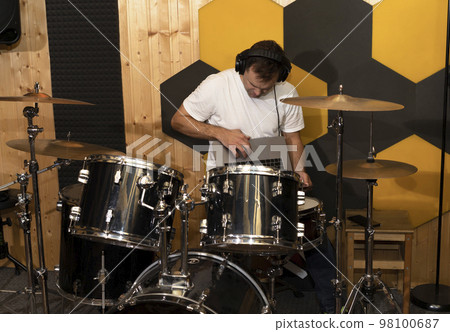 White Caucasian man connects drums, musical instrument and app on notebook, makes equipment setup in underground studio. Soundproofed wooden wall. Darken photo. Musical software. Horizontal 98100687