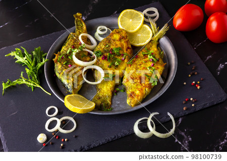 Fried Freshwater Fish with Lemon in a Plate on Black Slate Board. Fried Freshwater Fish with Lemon in a Plate on Black Slate Board. 98100739
