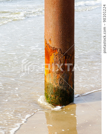 A vertical thick rusty metal pole on the seashore corroded by salty sea water 98101224