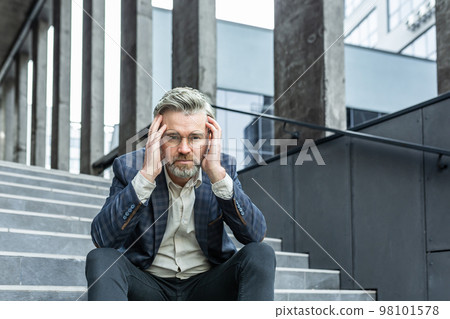 Gray haired businessman sitting sad on stairs outside office building, depressed boss in business suit upset and disappointed with achievement results. 98101578