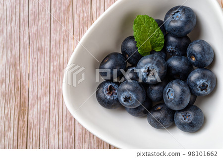 Ripe blueberry in white bowl over wooden surface. 98101662