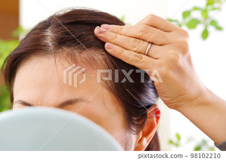 A woman in her 40s who makes a gesture to care about her hair 98102210