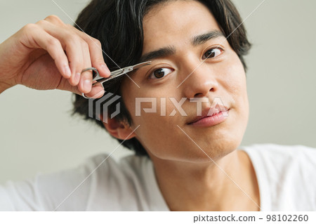 Young man trimming his eyebrows with scissors Young man trimming his eyebrows with scissors 98102260