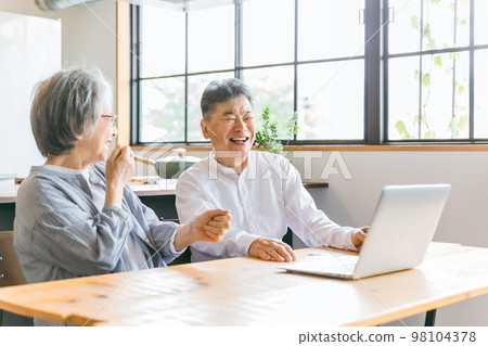 Elderly couple using a personal computer in the dining room at home (roar of laughter, video, movie, video call) 98104378