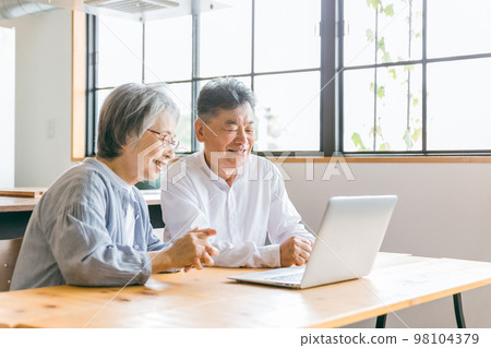 Elderly couple using a personal computer in the dining room at home (roar of laughter, video, movie, video call) 98104379