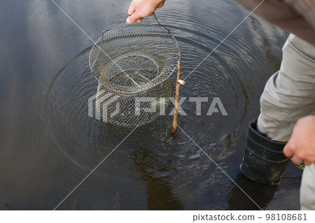 fisherman lifts a fish net. Metal mesh cage is installed in the river water near the shore. fisherman lifts a fish net. Metal mesh cage is installed in the river water near the shore. 98108681