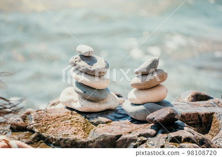 Woman with daughter bilds stones pyramid on seashore on a sunny day on the blue sea background. Happy family holidays. Pebble beach, calm sea. Concept of happy vacation on the sea, meditation, spa Woman with daughter bilds stones pyramid on seashore on a sunny day on the blue sea background. Happy family holidays. Pebble beach, calm sea. Concept of happy vacation on the sea, meditation, spa 98108720