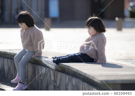 Girl sisters sitting on a park bench 98109493