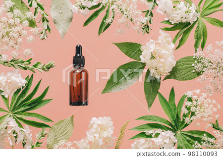 Cosmetic amber glass dropper bottle in fresh nature setup. Green leaves white flowers on peach pink. Essential aroma oil or face care serum essence. natural beauty and cosmetics. Pink forest Cosmetic amber glass dropper bottle in fresh nature setup. Green leaves white flowers on peach pink. Essential aroma oil or face care serum essence. natural beauty and cosmetics. Pink forest 98110093