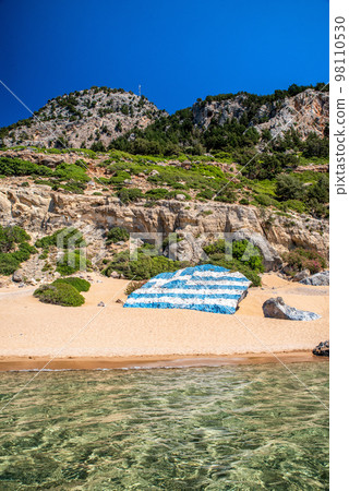 Big greek flag painted on large rock at Tsambika beach at Rhodes island in Greece 98110530