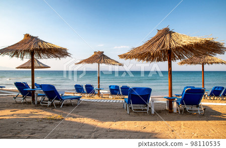Empty loungers under sunshades on sandy beach with view on sea 98110535