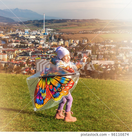 Girl flying a kite in a field over town Girl flying a kite in a field over town 98110874