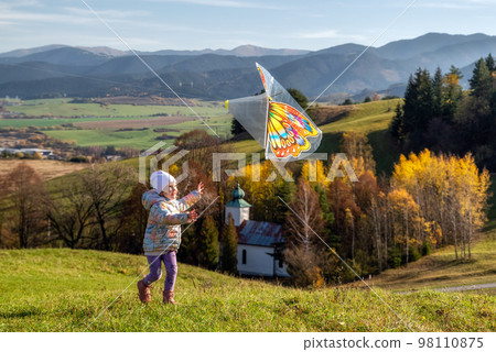 Small girl running with colorful kite t sunset among plant field Small girl running with colorful kite t sunset among plant field 98110875
