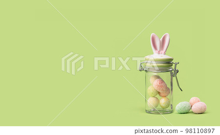 Easter bunny ears sweets jar with many tiny eggs in and near on spring yellow green edgeless background. Happy Easter holiday concept. Easter chocolate treats web wide banner Easter bunny ears sweets jar with many tiny eggs in and near on spring yellow green edgeless background. Happy Easter holiday concept. Easter chocolate treats web wide banner 98110897