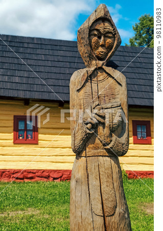 Wooden statue of villager in front of picturesque historical village Vlkolinec witjh wooden colorful cottages in Slovakia 98110983