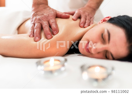 Masseur massaging back and shoulder blades of young woman lying on massage table on white background. Concept of massage spa treatments 98111002
