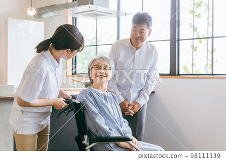 An elderly couple sitting in a wheelchair and a caregiver, physical therapist, and nursing care staff woman 98111139