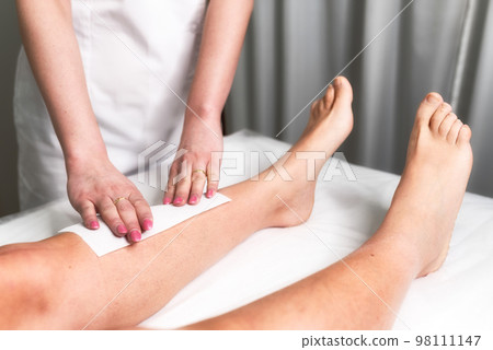 Beautician waxing a woman's leg applying a strip of material over the hot wax to remove the hairs 98111147