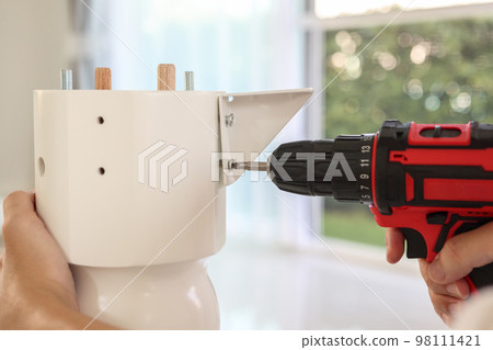 man assembling white table furniture at home using cordless screwdriver 98111421