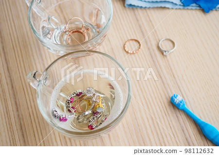 cleaning jewelry diamond ring with glass of hot water and dishwashing liquid on wood table background cleaning jewelry diamond ring with glass of hot water and dishwashing liquid on wood table background 98112632
