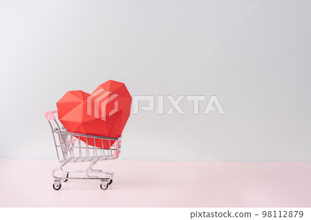 Red paper heart in a shopping cart against blue background 98112879