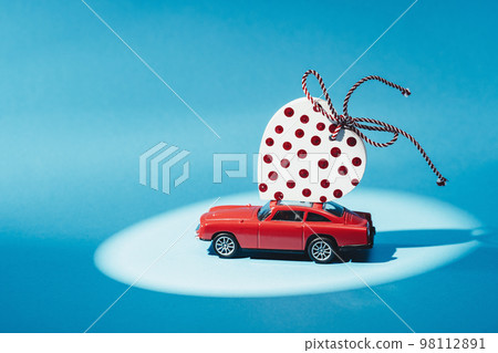 Red retro toy car delivering polka dot craft heart on roof top on blue background. St Valentines Day thank you card Mothers or Fathers Day. Birthday gift or sales delivery Red retro toy car delivering polka dot craft heart on roof top on blue background. St Valentines Day thank you card Mothers or Fathers Day. Birthday gift or sales delivery 98112891