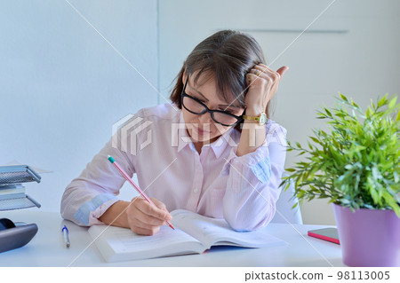 Middle-aged female working at home at table with books 98113005