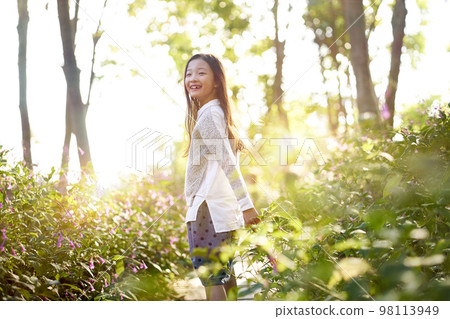 8 year-old beautiful little asian girl standing in flower field looking back and smiling 98113949