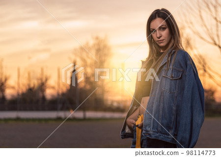 Portrait of young blonde woman posing looking at camera with denim jacket on her shoulders at sunset Portrait of young blonde woman posing looking at camera with denim jacket on her shoulders at sunset 98114773