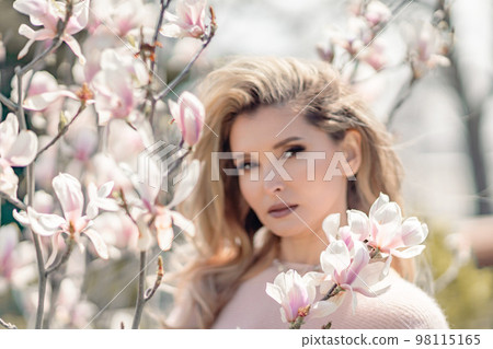Portrait of a beautiful happy middle aged woman enjoying the smell in a blooming spring garden. Beautiful magnolia bushes, large flowers. Portrait of a beautiful happy middle aged woman enjoying the smell in a blooming spring garden. Beautiful magnolia bushes, large flowers. 98115165