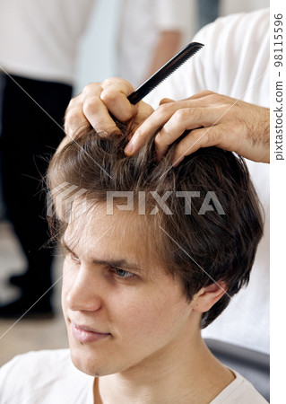 close-up, professional male hairstylist combing young customer's hair in barbershop close-up, professional male hairstylist combing young customer's hair in barbershop 98115596