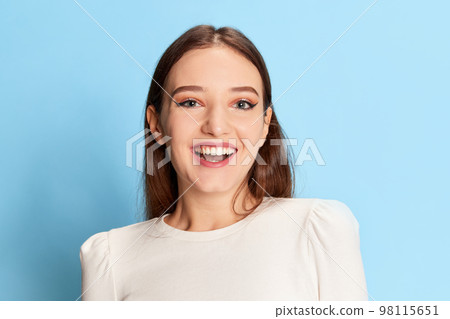 Portrait of young beautiful girl in casual clothes posing, smiling over blue studio background. Concept of emotions, lifestyle, youth 98115651