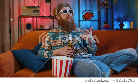 Man sitting on couch eating chips and watching interesting TV serial, sport game online at home 98115796
