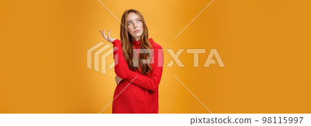 Portrait of unsure thinking redhead girlfriend in red sweater looking uncertain at upper left corner, recalling, feeling nostalgic, solving puzzle in mind, posing against orange background Portrait of unsure thinking redhead girlfriend in red sweater looking uncertain at upper left corner, recalling, feeling nostalgic, solving puzzle in mind, posing against orange background 98115997