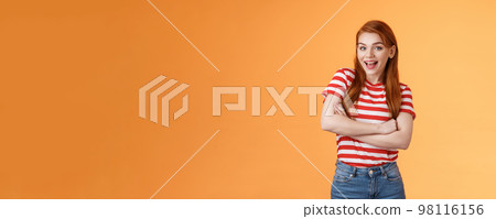 Excited cheerful ginger girl long natural red hair open mouth enthusiastic smile, cross arms chest, gladly react interesting awesome news, feel surprised pleased, stand orange background 98116156